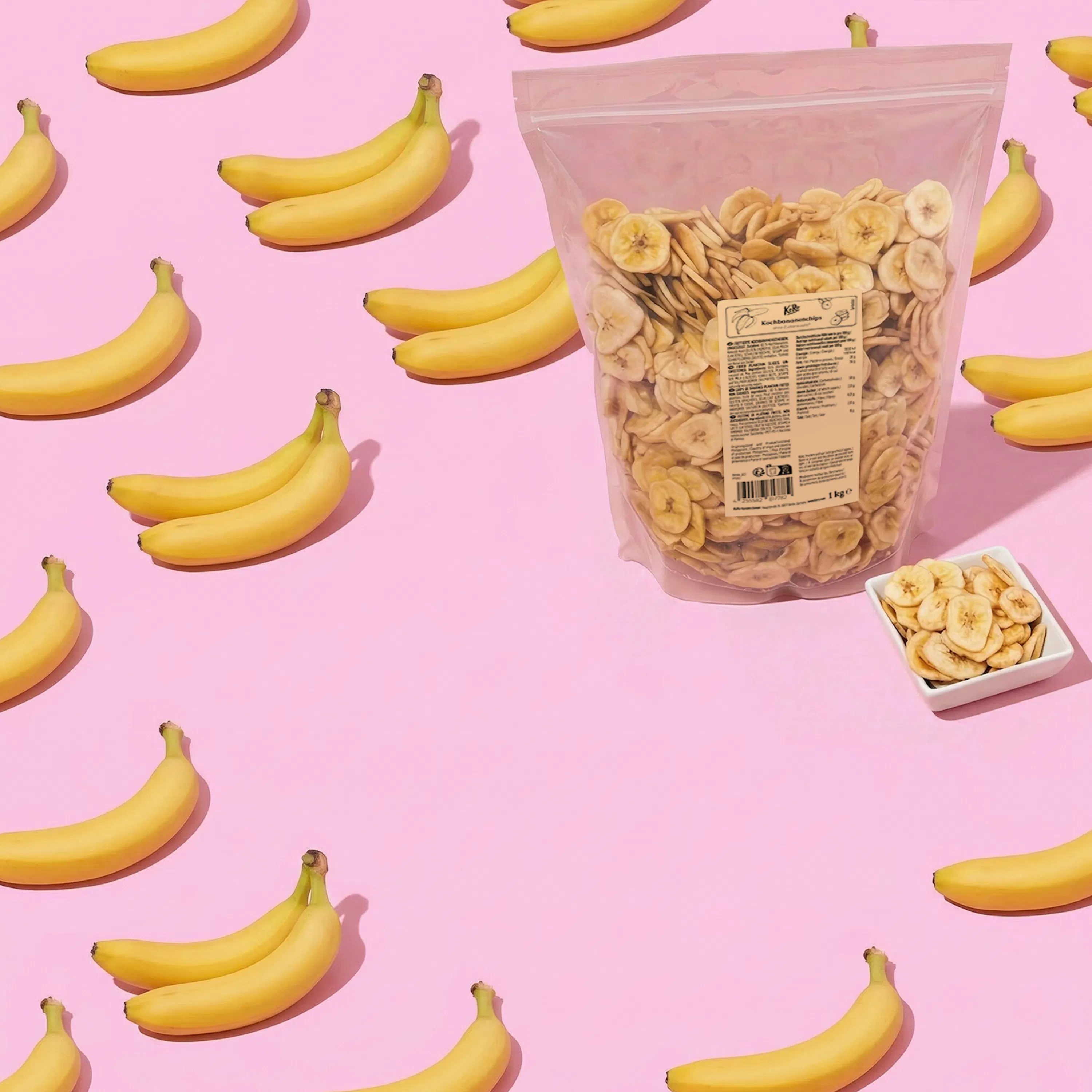 ein rosa hintergrund mit frischen bananen und einer tüte sowie einer schale mit bananenchips.