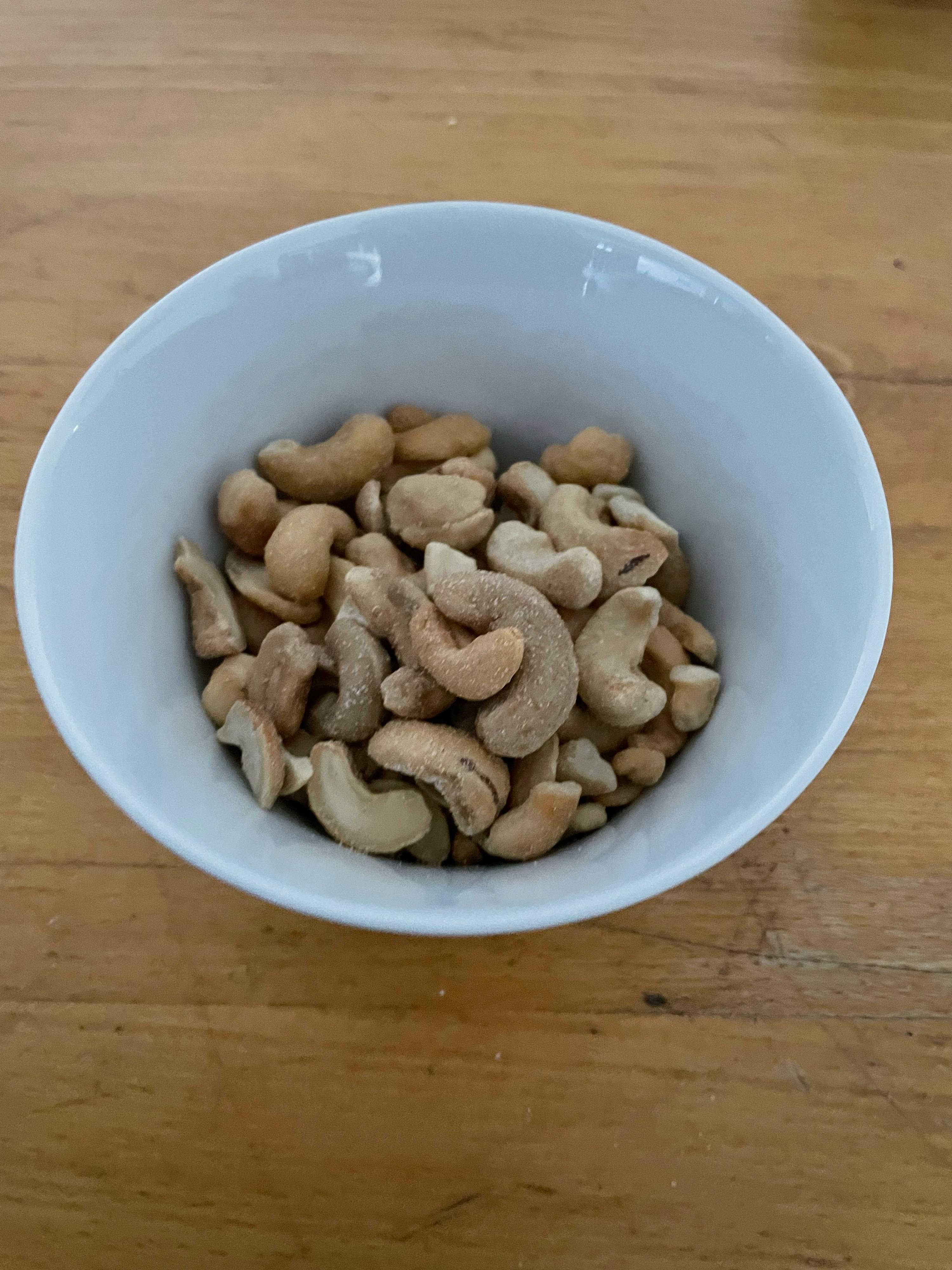 eine weiße Schüssel mit cashewkernen auf einem Holztisch