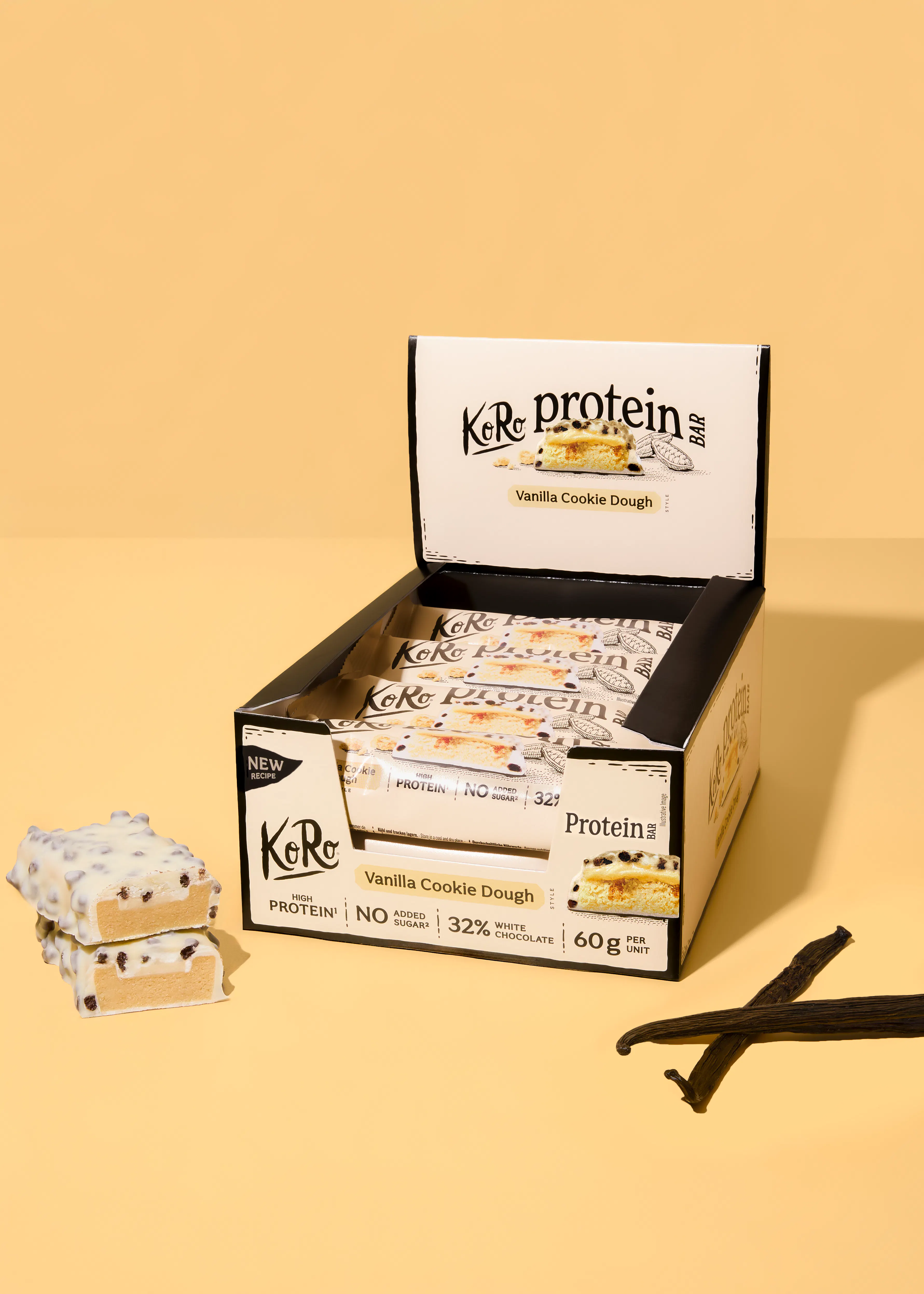 an open box of koro protein vanilla cookie dough bars, with two unwrapped bars and vanilla pods, all on a yellow surface.