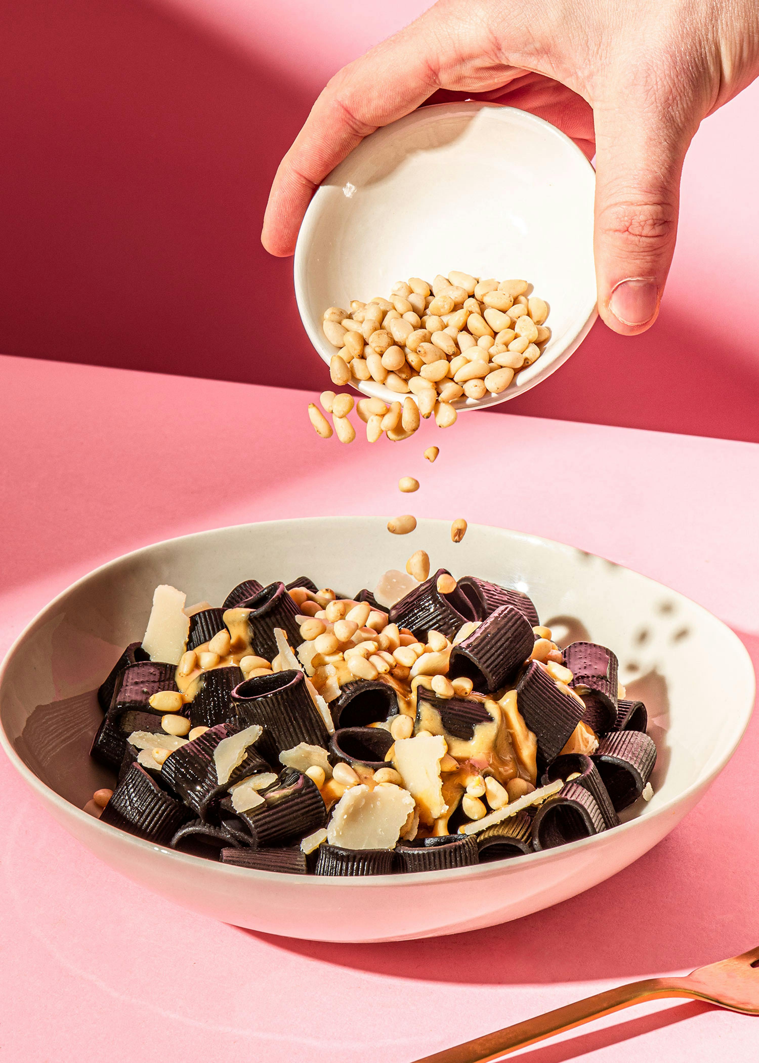 a person is pouring pine nuts into a bowl of pasta