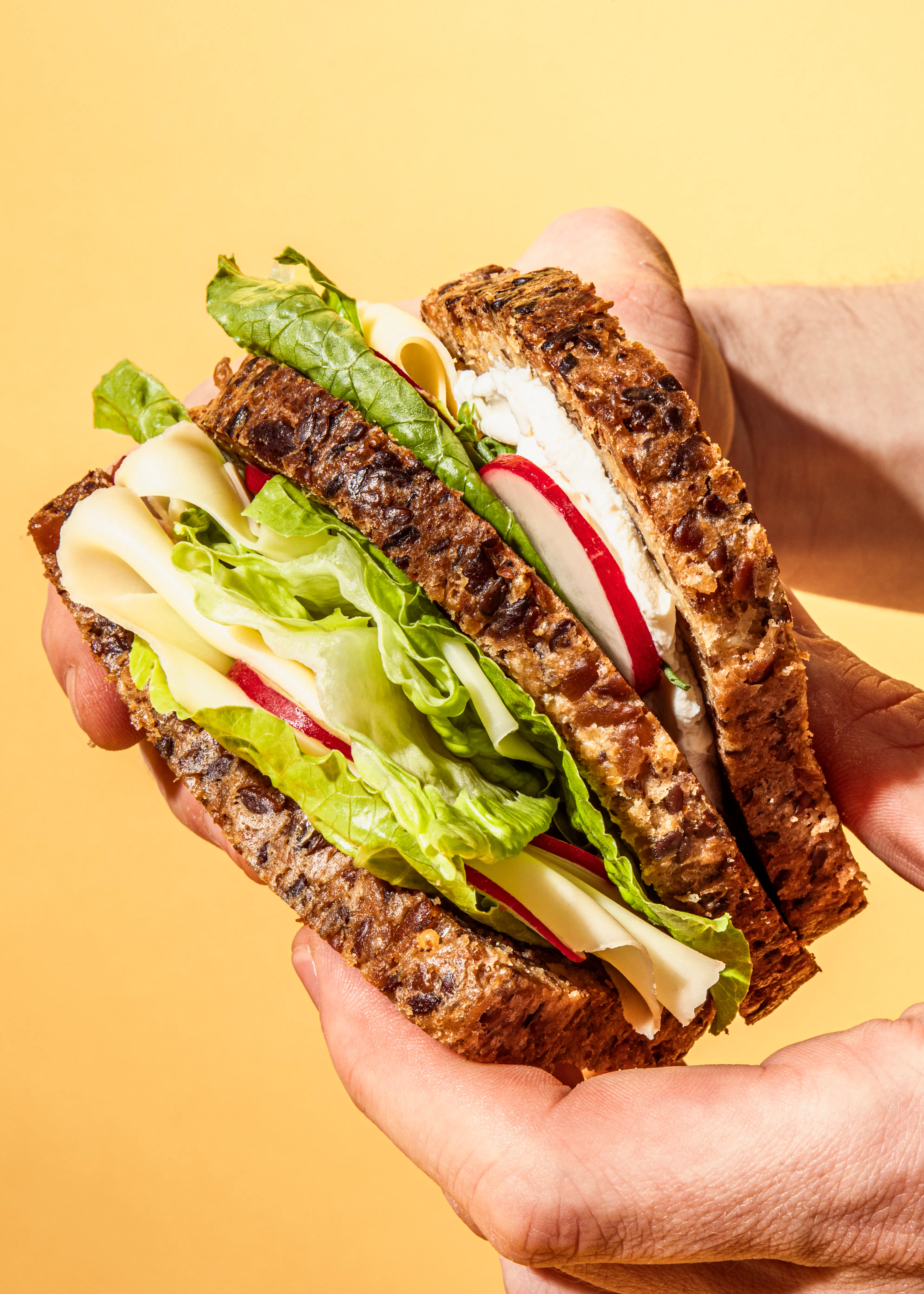 eine Person hält ein Sandwich mit Salat und Käse