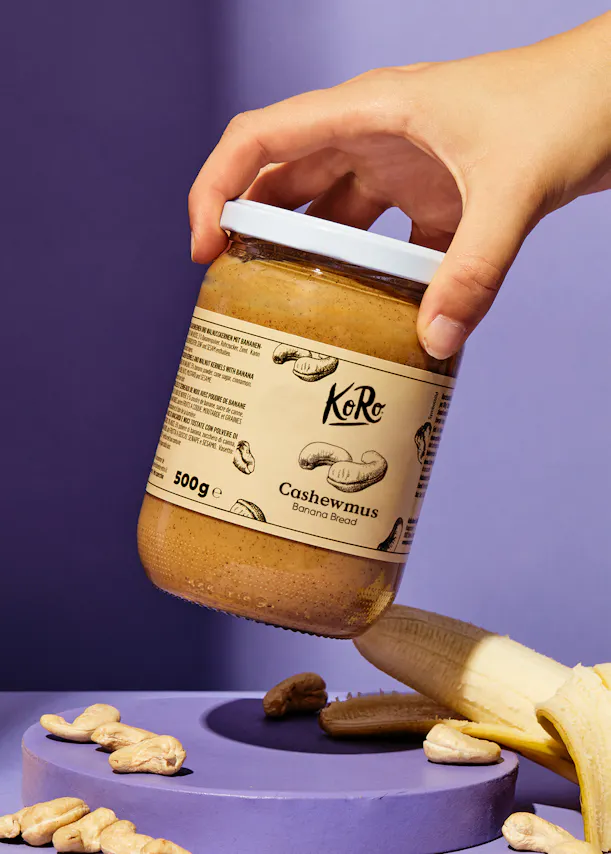 une personne tient un pot de beurre de noix de cajou à côté d' une banane