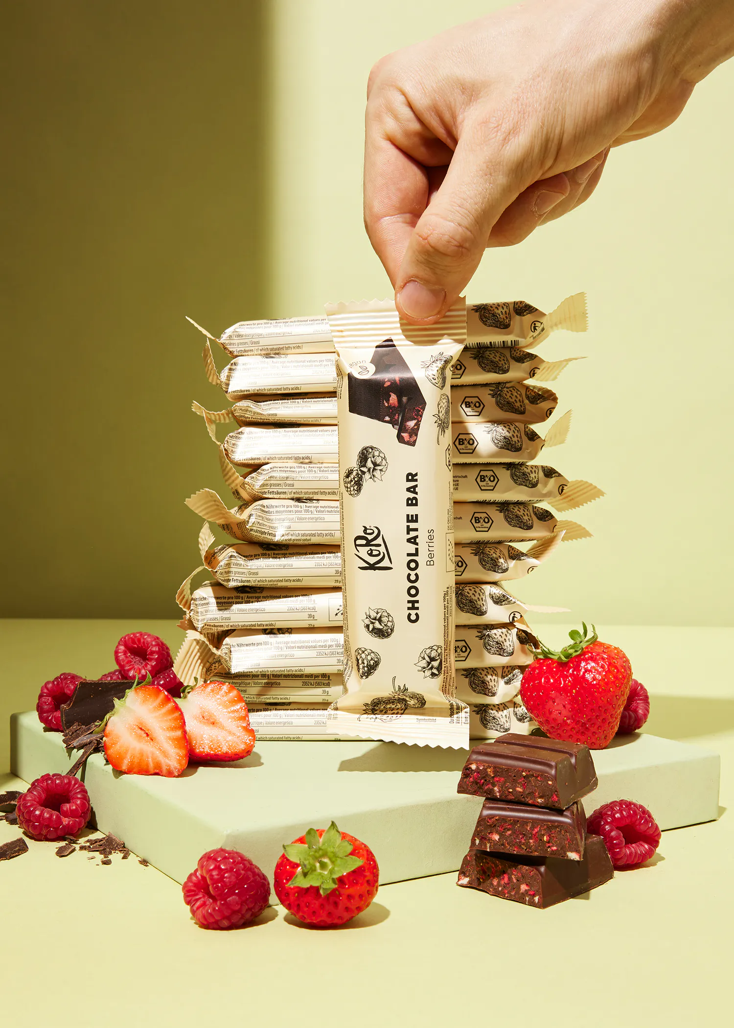 une barre de chocolat est posée sur une table entourée de fraises et de framboises