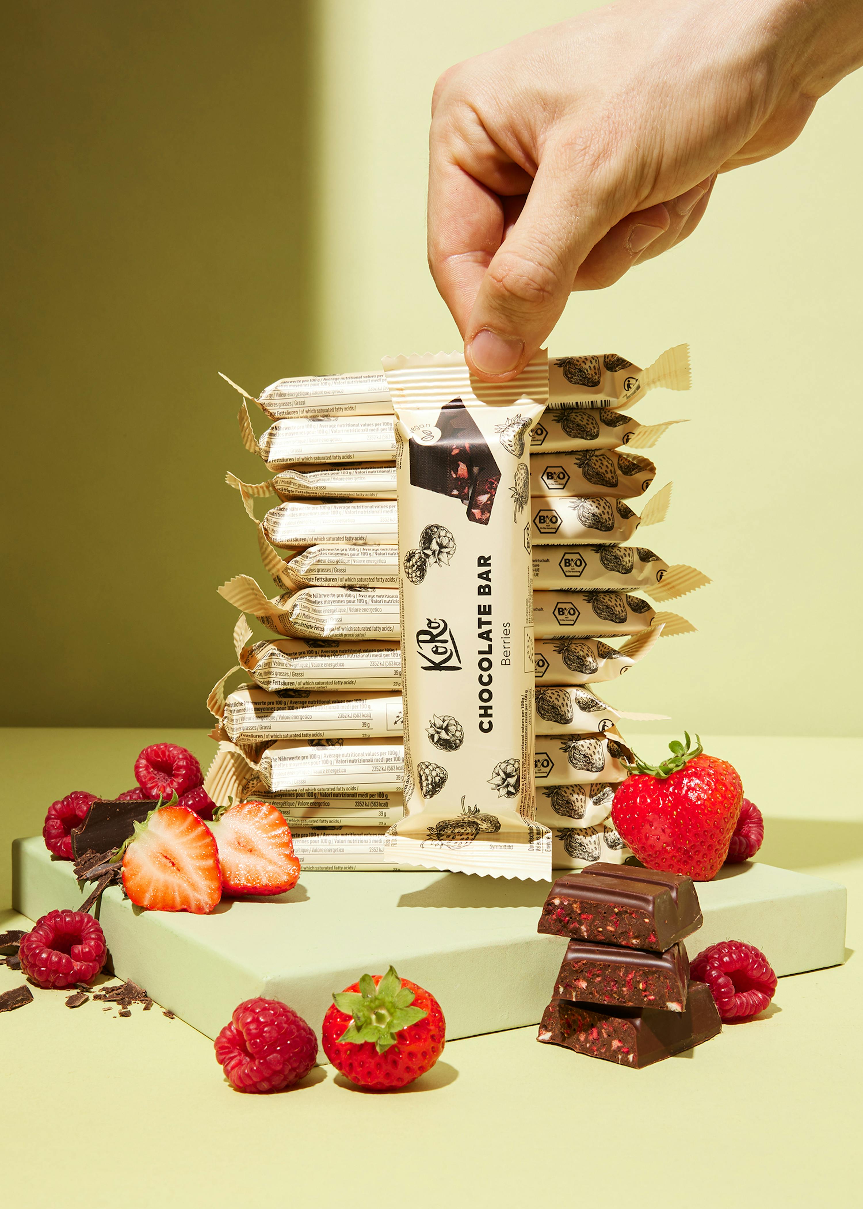 une barre de chocolat est posée sur une table entourée de fraises et de framboises