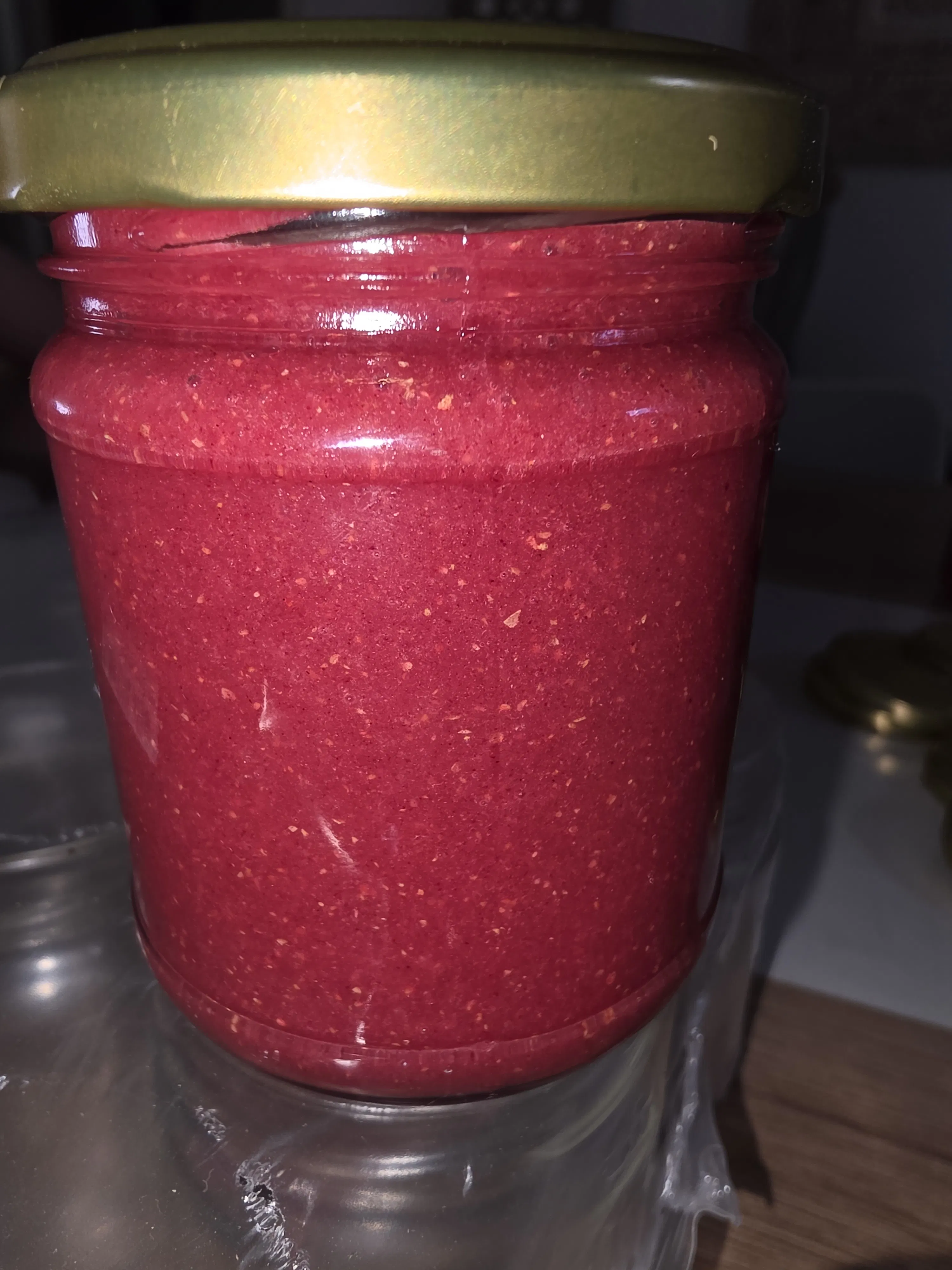 un barattolo di vetro chiuso con un tappo dorato contenente una crema spalmabile di colore rosso intenso.