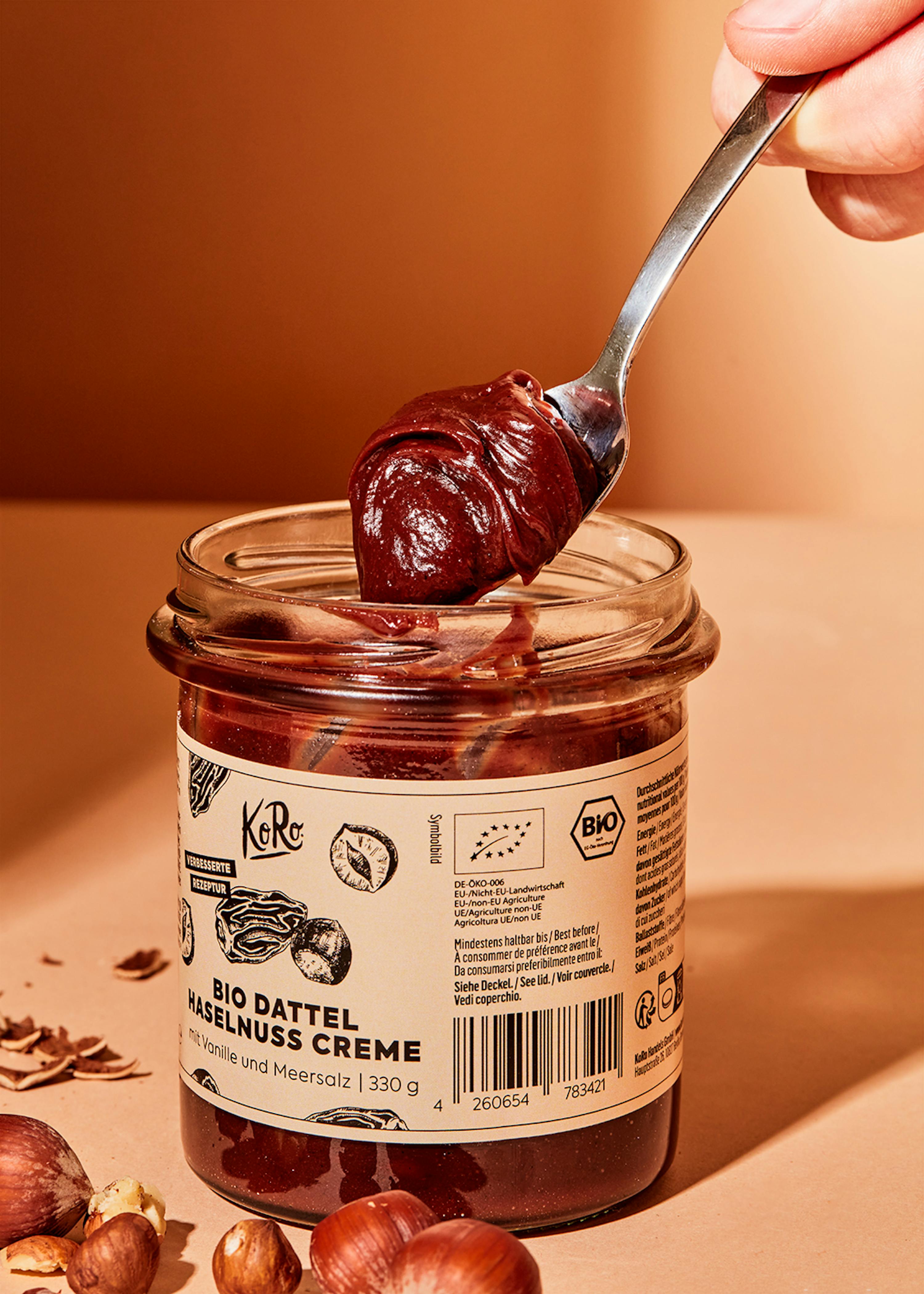 eine Person hält einen Löffel aus einem Glas bio dattel-haselnuss-creme
